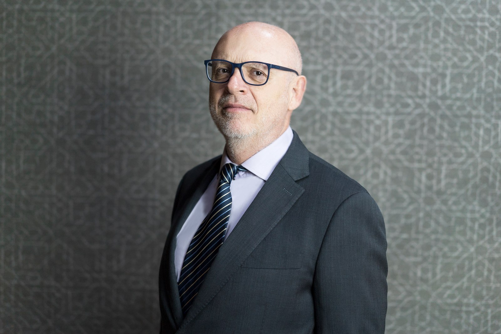 Corporate headshot of a man with glasses in a dark suit and tie