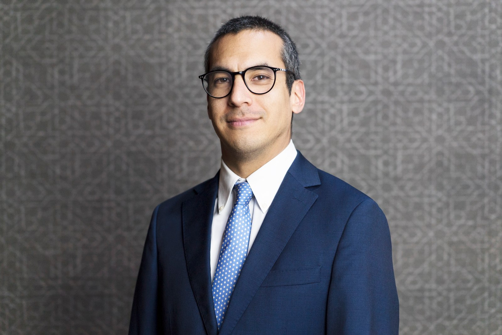 Corporate headshot of a man with glasses in a navy suit