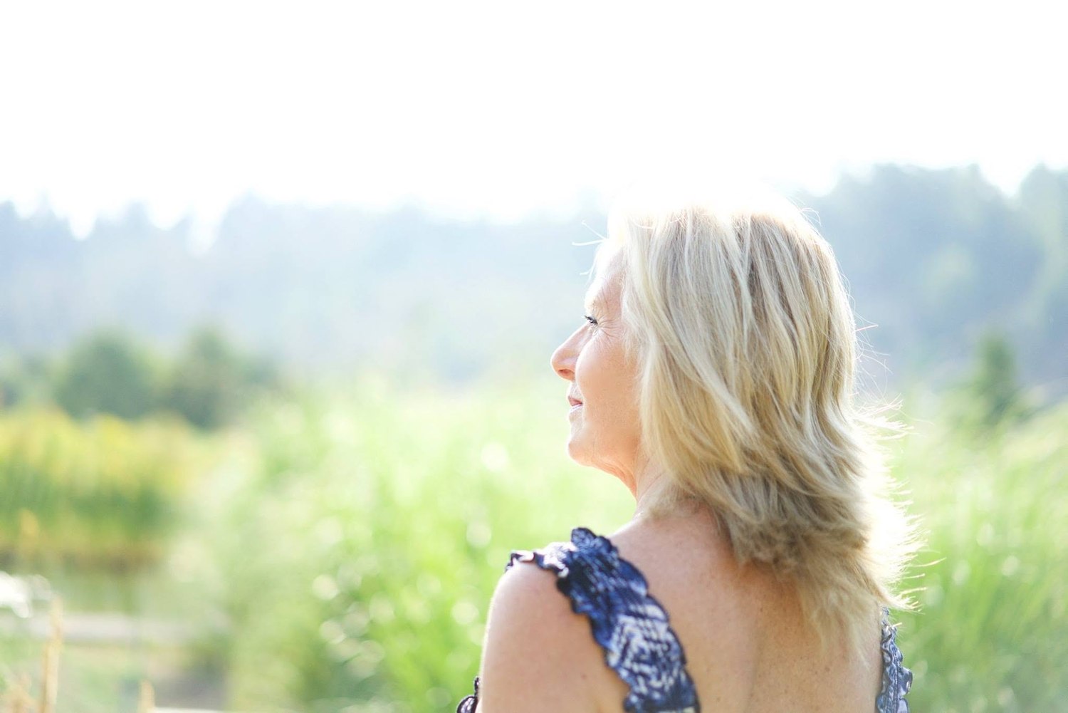 Portrait of a woman in profile outdoors, backlit by sunlight over a green field