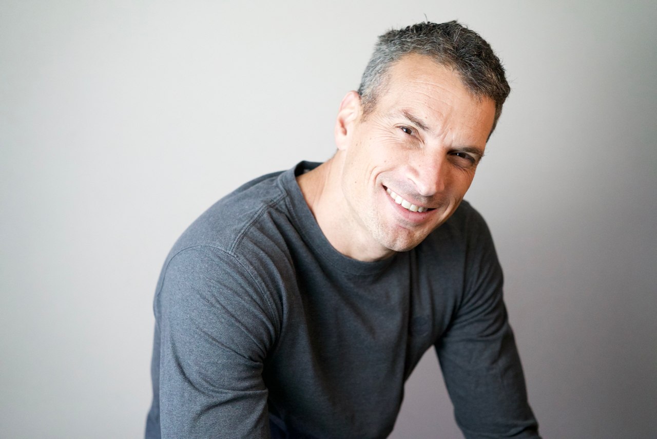 Portrait of a smiling man in a grey shirt leaning forward