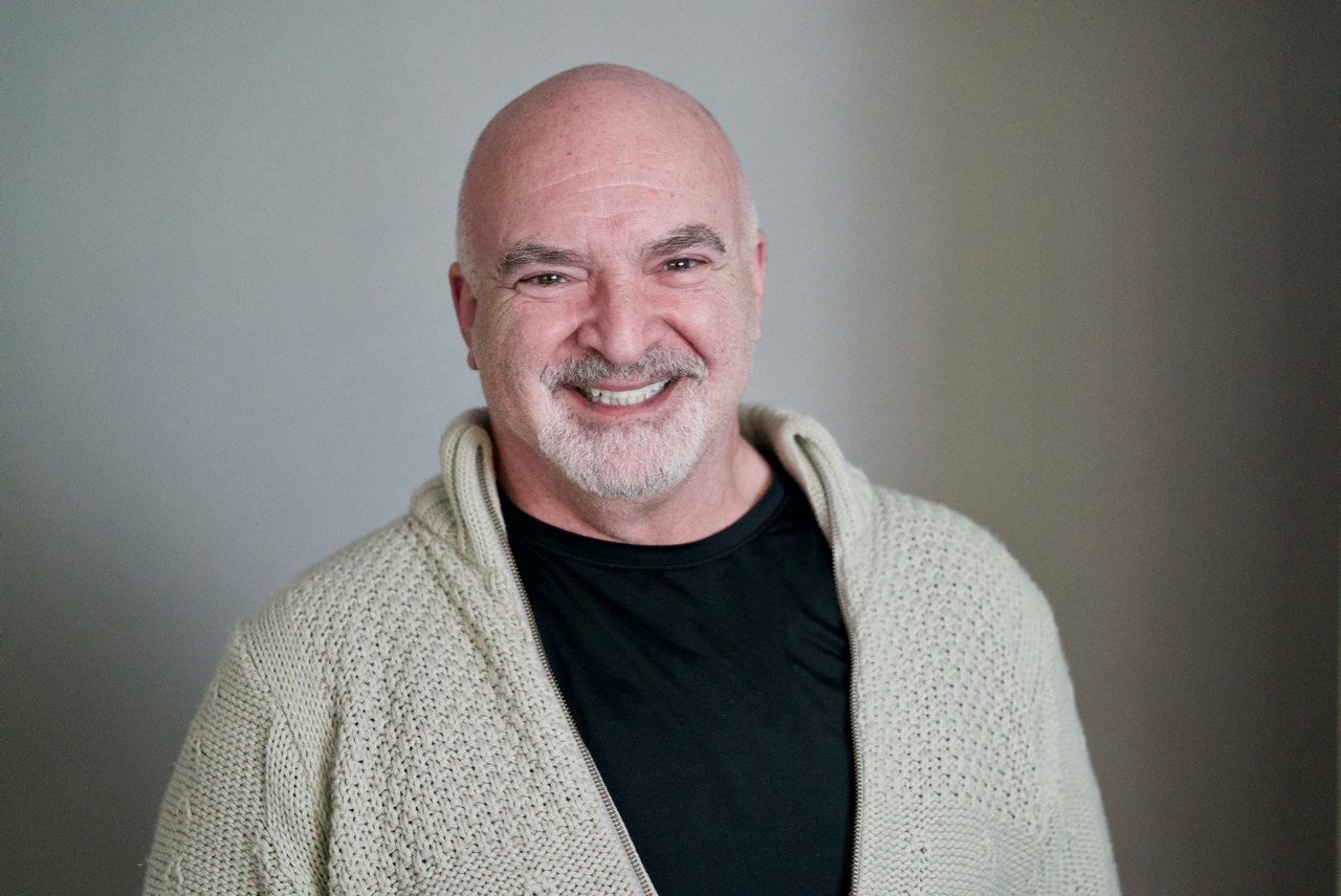 Portrait of a smiling bald man with a beard, wearing a cream cardigan